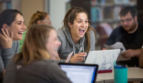 a group of students working together on laptops and smiling