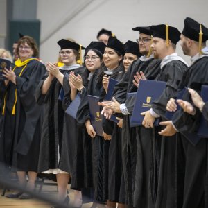 people in commencement gowns applaud and smile