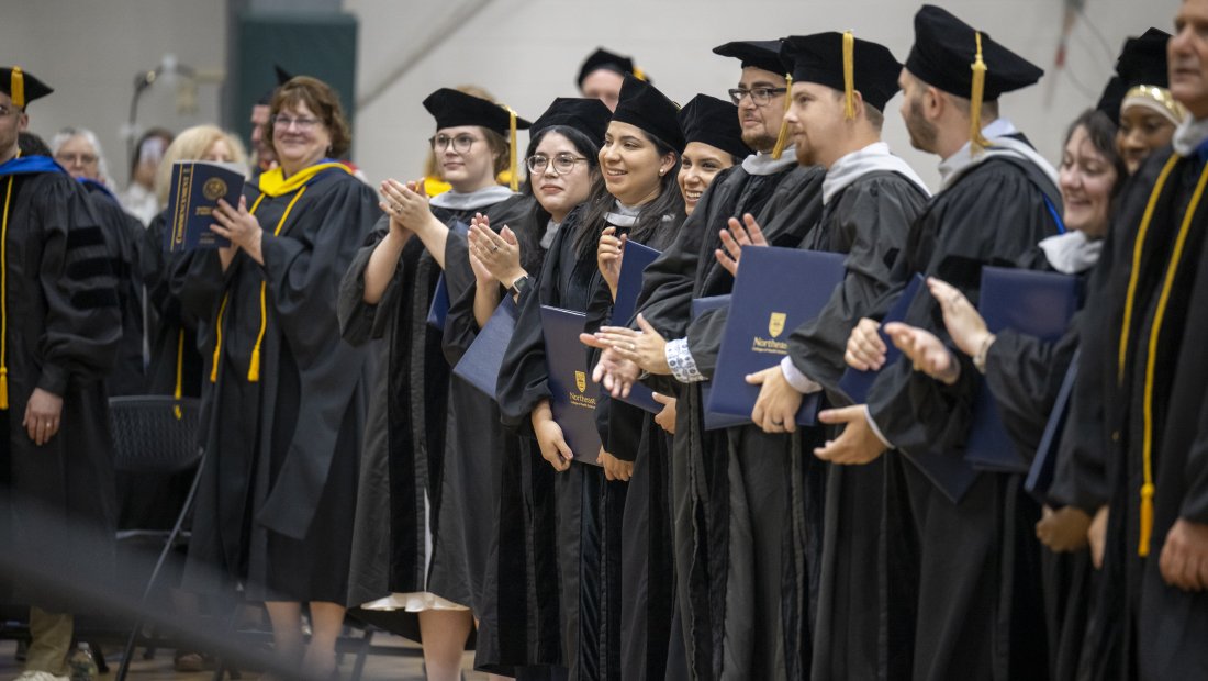 people in commencement gowns applaud and smile