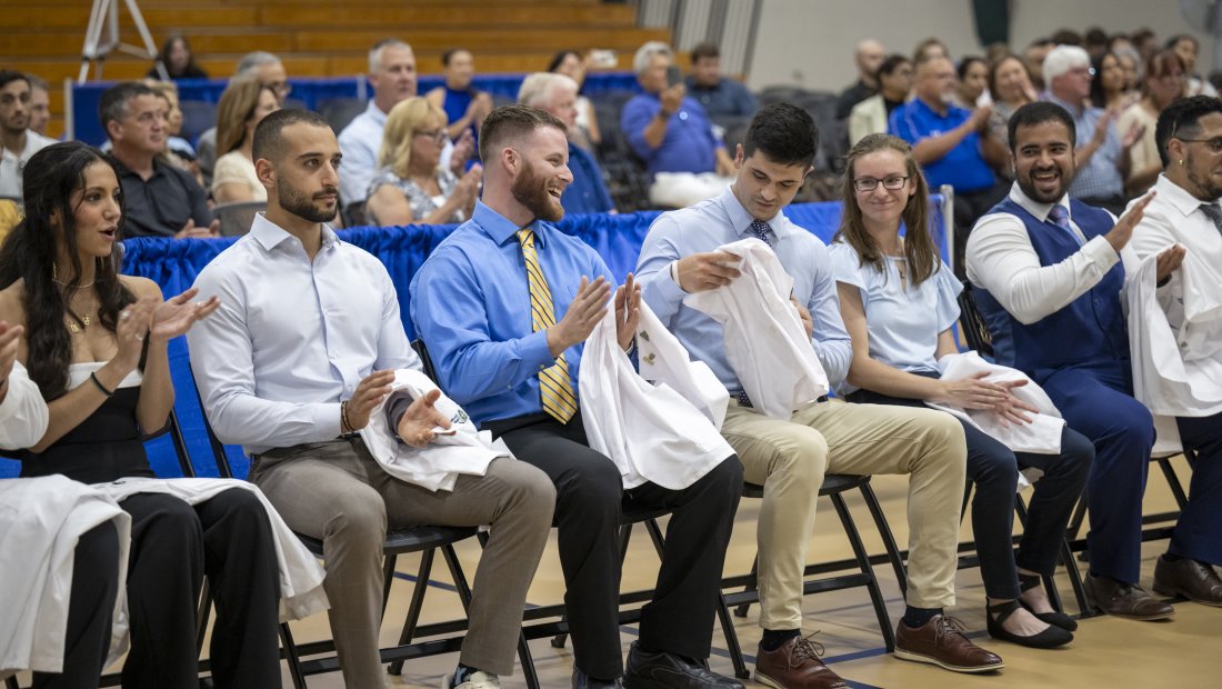 students clapping and smiling, holding their white coats