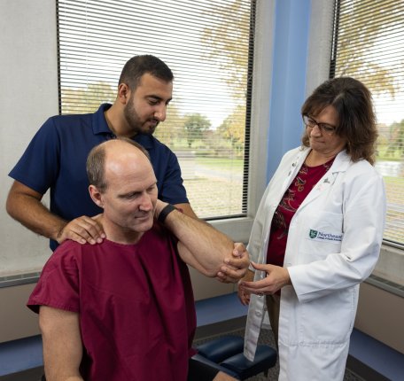 a chiropractic student and instructor work with a patient in a clinical setting